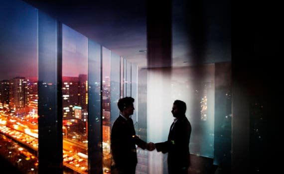 Businessmen shaking hands in office at night with city view