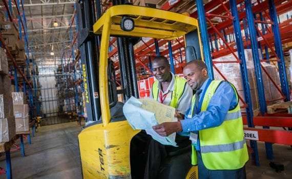 Two men next to a forklift pointing at paperwork